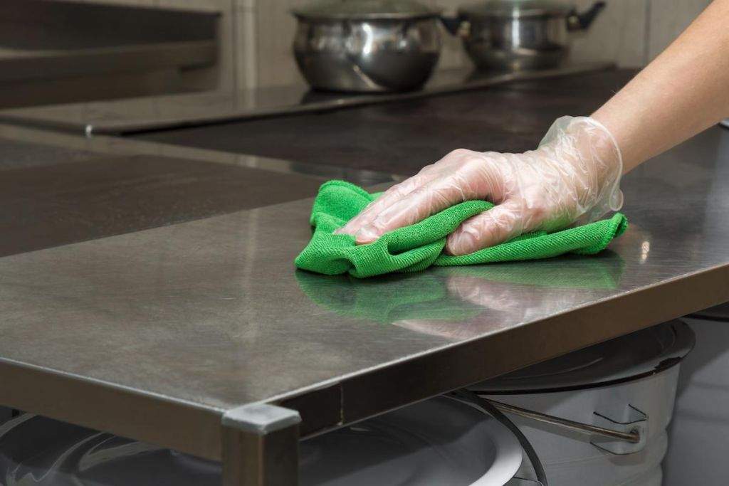 persons hand with a glove on cleaning a stainless steel kitchen surface with a rag